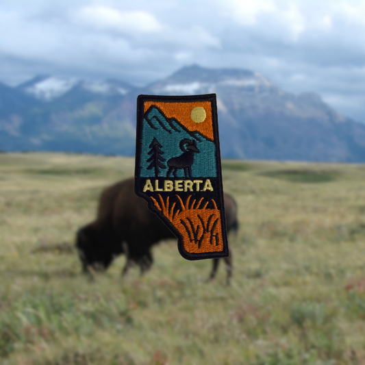 Embroidered patch with 'Alberta' text and mountain design over a blurred natural background